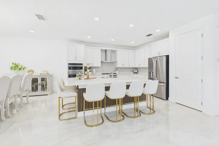 Open-concept kitchen with a large central island, white cabinetry, integrated double wall ovens, stainless steel refrigerator, and light-toned tile flooring