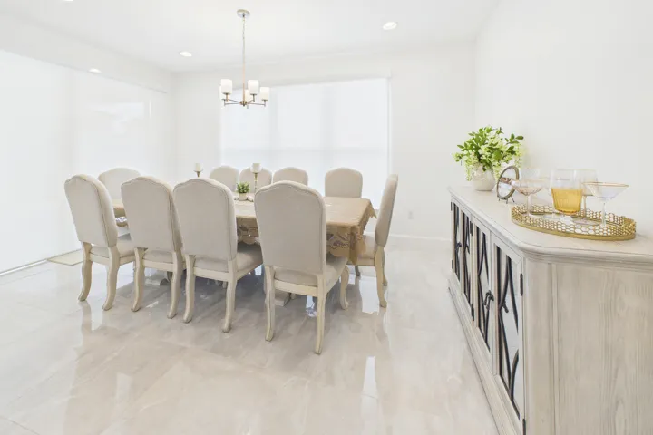 Recessed lighting, chandelier, and large window with roller shades illuminate a room featuring light-toned tile flooring and a built-in buffet cabinet