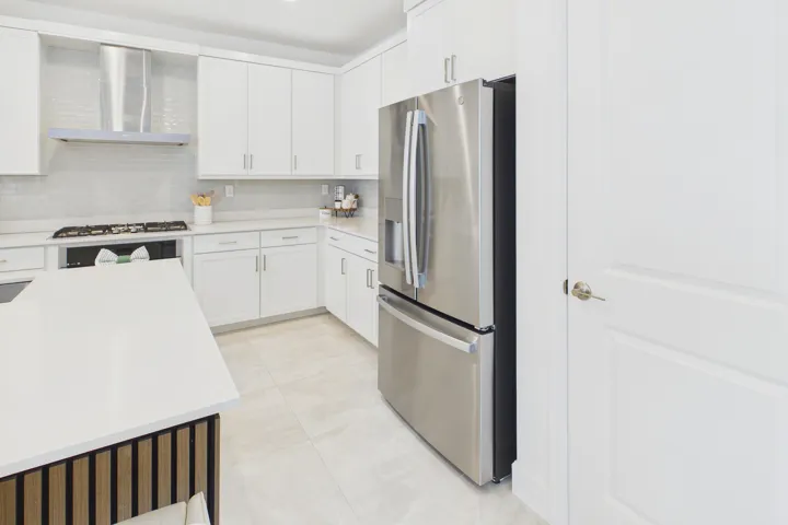 Kitchen featuring white cabinetry, stainless steel appliances, a tile backsplash, and a central island with wood-finish paneling