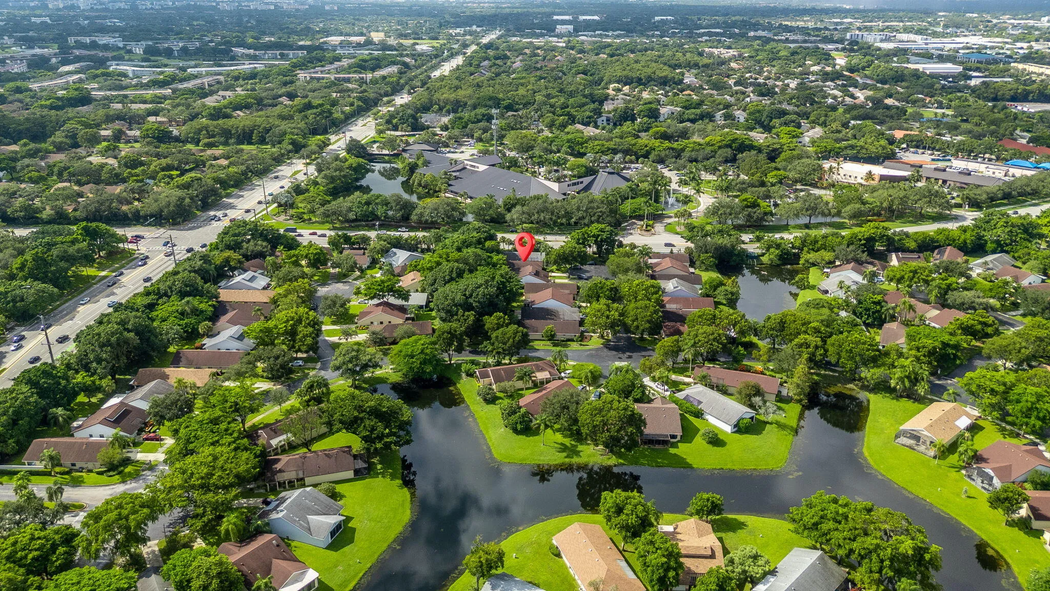 Aerial view of a residential area featuring multiple single-story homes, lush green landscaping, and prominent water features