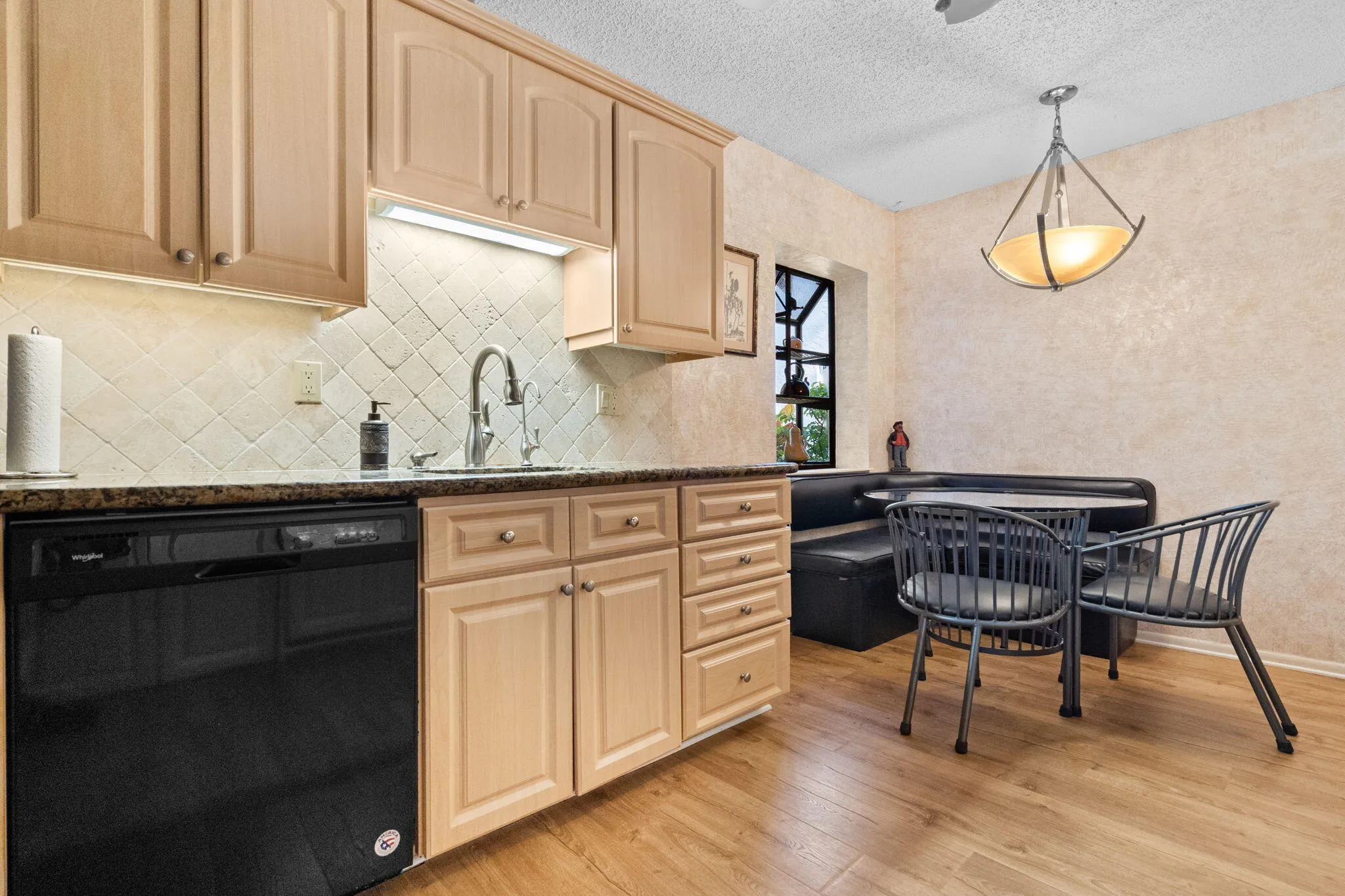 Kitchen with wood-finish flooring, light-toned cabinetry, a built-in black dishwasher, and a dark countertop