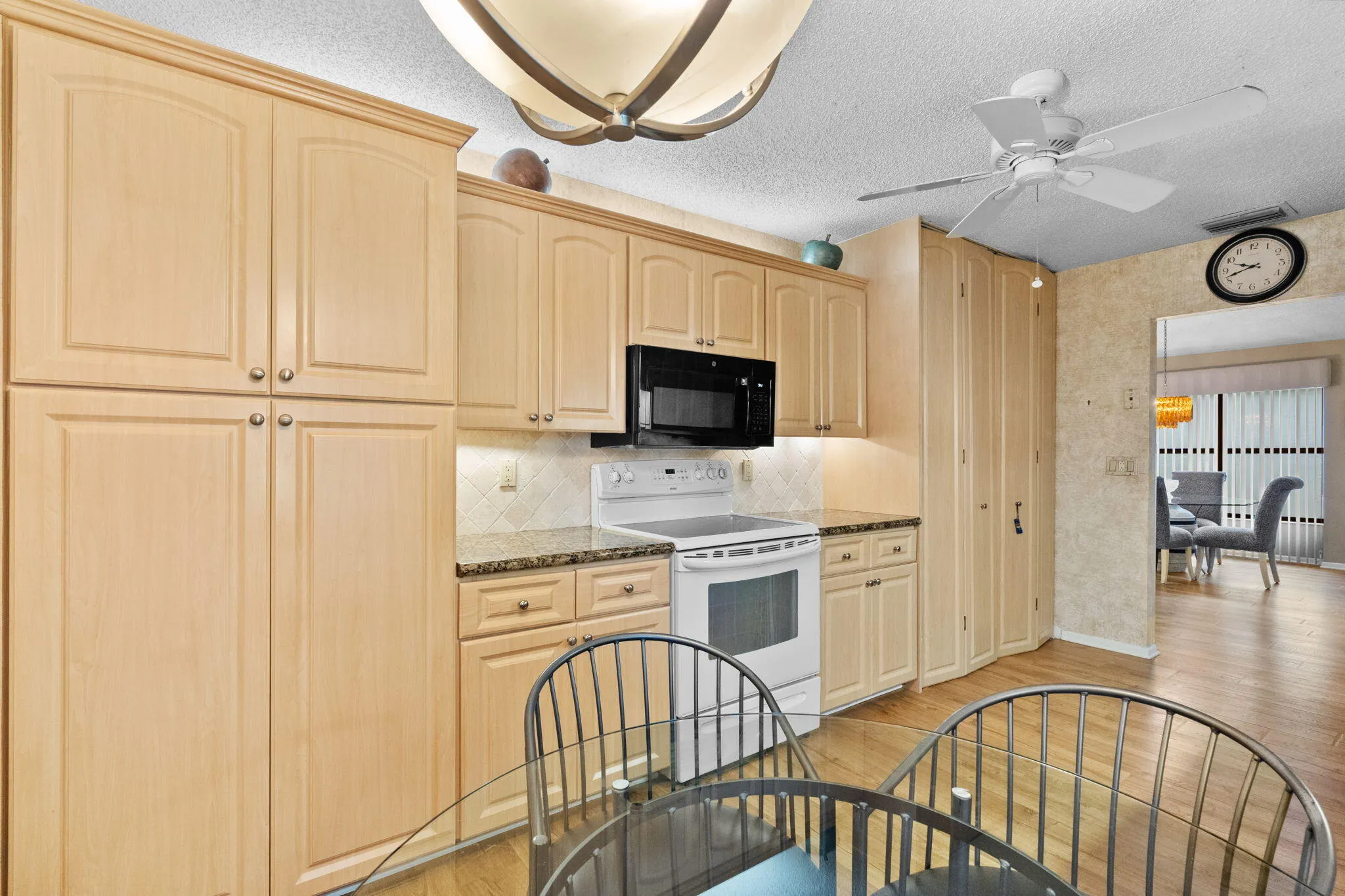 Full kitchen with light wood-finish cabinetry, black appliances, white electric range, and speckled countertops