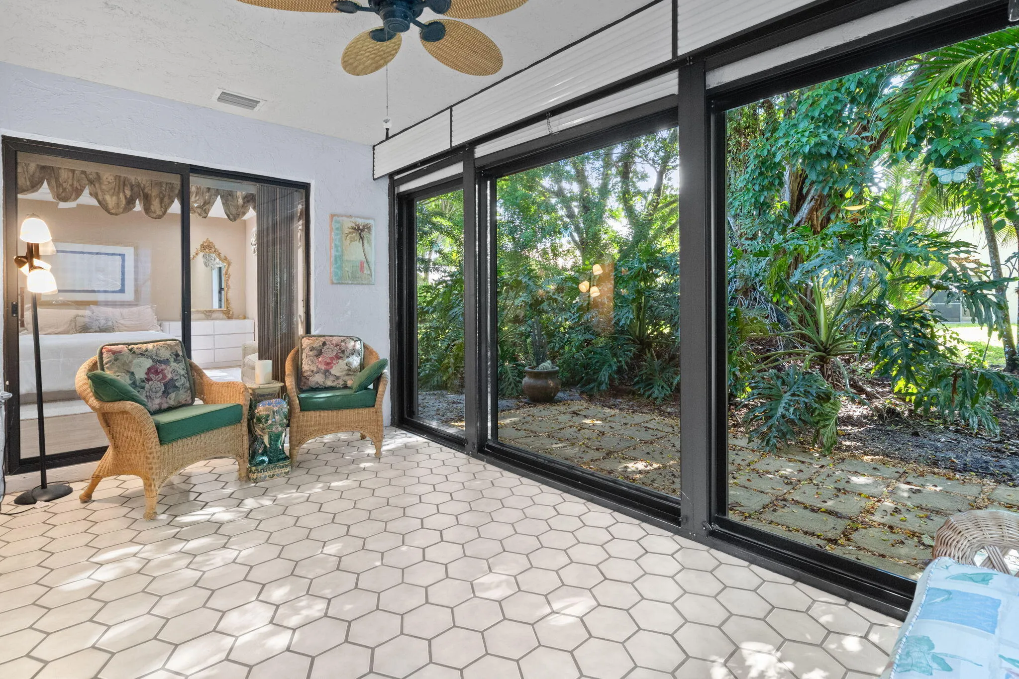 Hexagonal tile flooring, sliding glass doors, built-in ceiling fan, and large windows overlooking the exterior foliage
