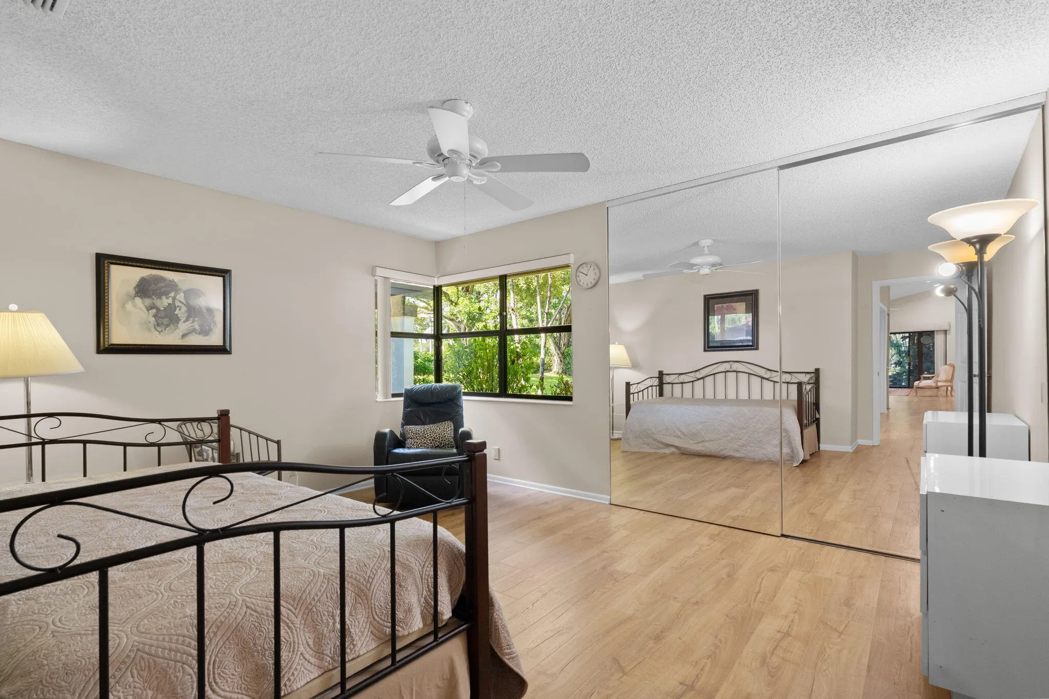 Wood-finish flooring, mirrored closet doors, a ceiling fan, and a large window