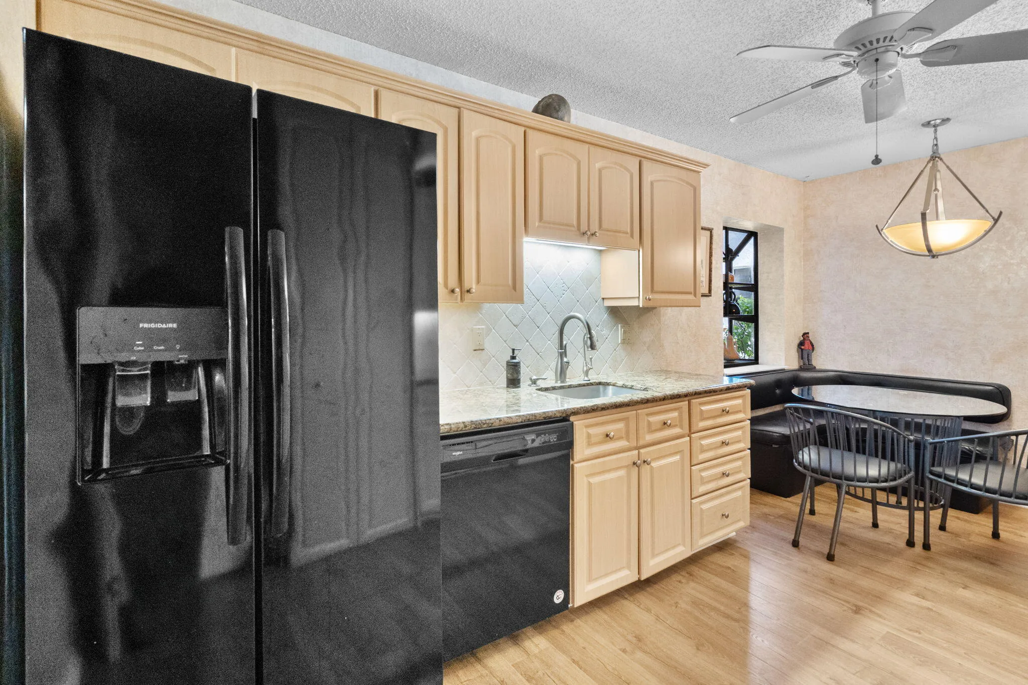 Kitchen featuring wood-finish flooring, a black side-by-side refrigerator, light-toned cabinetry, granite countertops, and a built-in banquette