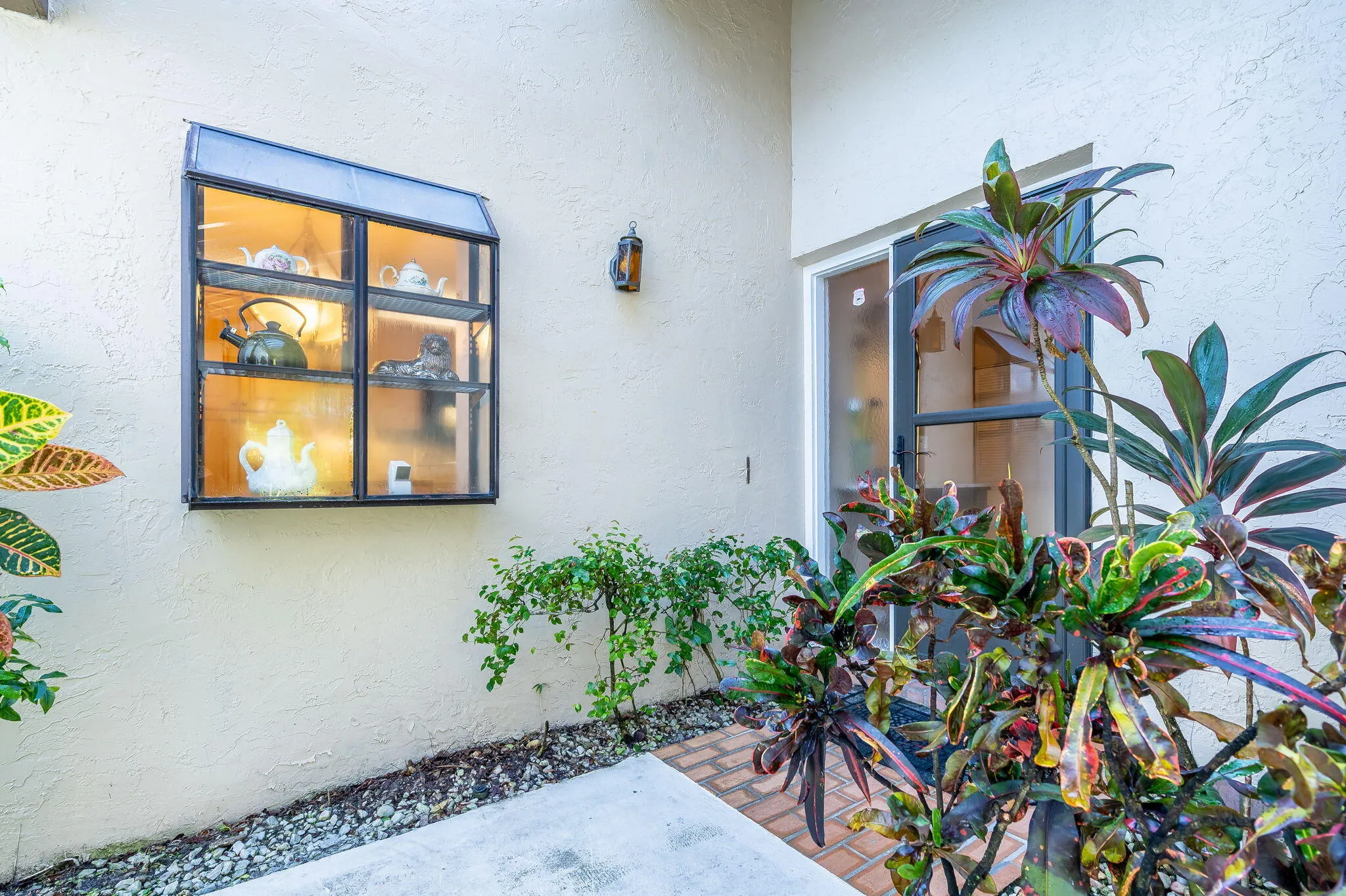 Stucco exterior with a display window featuring shelving, a modern wall-mounted light fixture, and a sliding glass entry door