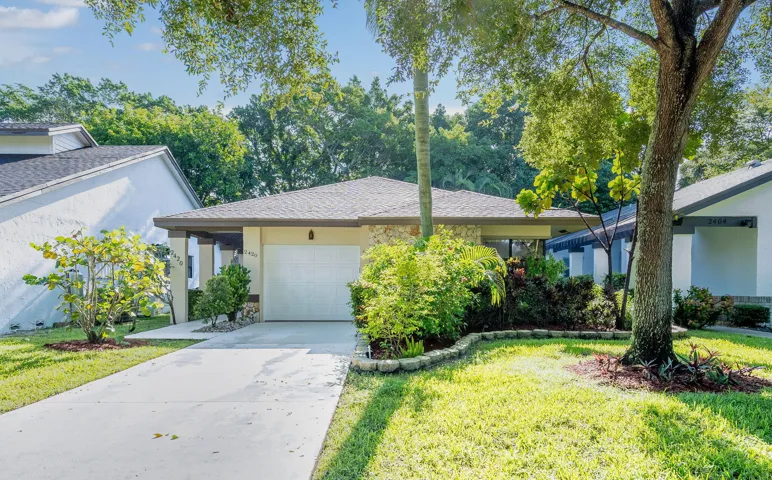 Single-story residence featuring a garage, mature trees, and established landscaping