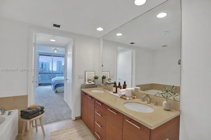 Dual vanity with undermount sinks and wood-finish cabinetry, full-width wall mirror, and built-in tub