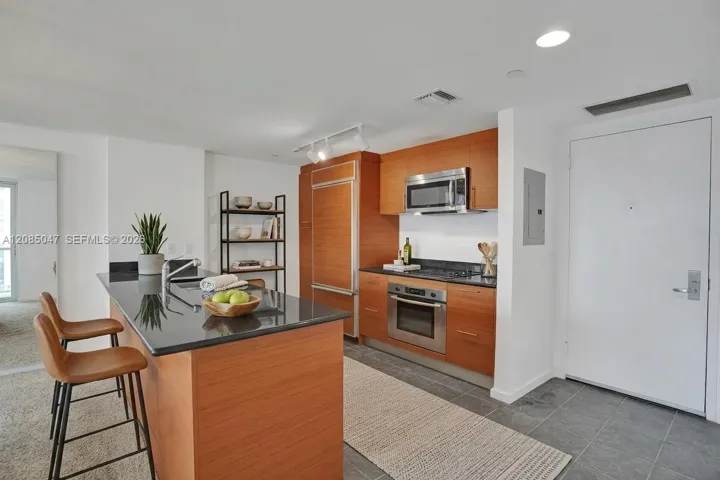 Kitchen featuring wood cabinetry, stainless steel appliances, a center island with a dark countertop, and tile flooring - virtually staged