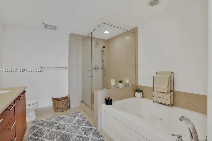 Glass-enclosed shower, built-in bathtub, light-toned wall tile, recessed ceiling lighting, and a floating vanity with a light-colored countertop virtually staged