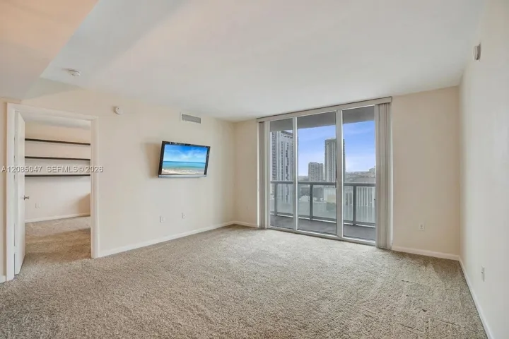 Carpeted living area featuring a full-height glass sliding door, balcony with metal railing, and built-in wall shelving in an adjacent room