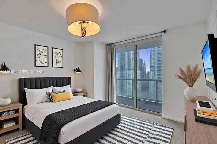 Sliding glass door leading to a balcony, modern flush mount ceiling light, two wall-mounted sconces, and light wood-finish nightstands virtually staged