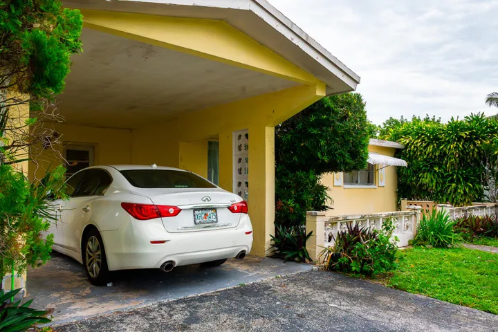 Covered carport with a concrete slab, painted exterior, and mature landscaping