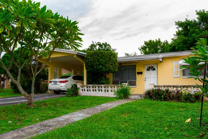 Exterior featuring a yellow facade, covered carport, and a white front door
