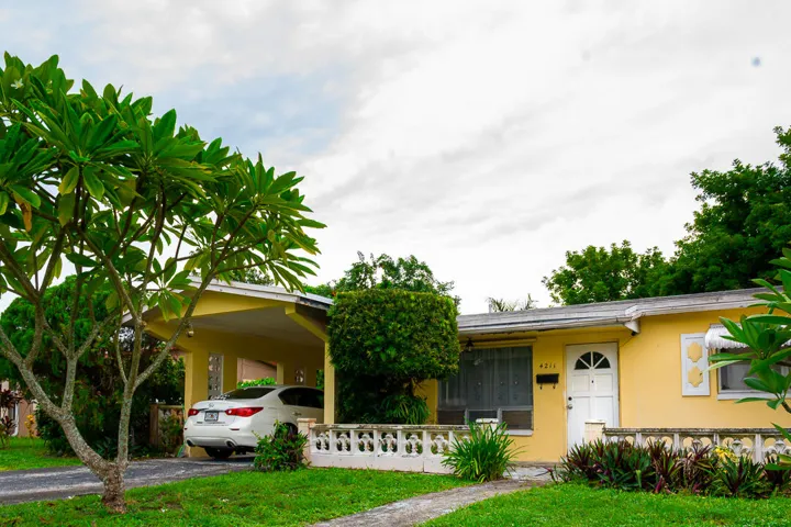Yellow exterior with a covered carport, concrete driveway, and front walkway