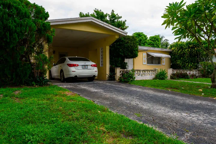 Single-story exterior with a covered carport, mature landscaping, and a paved driveway