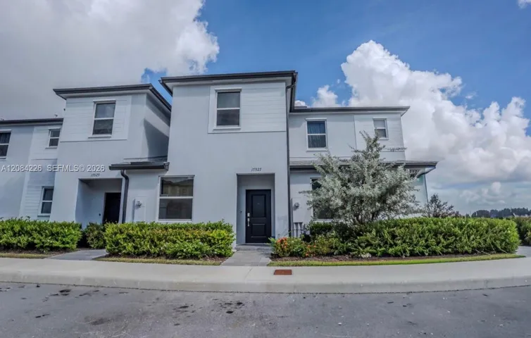 Multi-level exterior featuring a light-toned stucco finish, horizontal siding accents, dark-framed windows, and concrete walkways