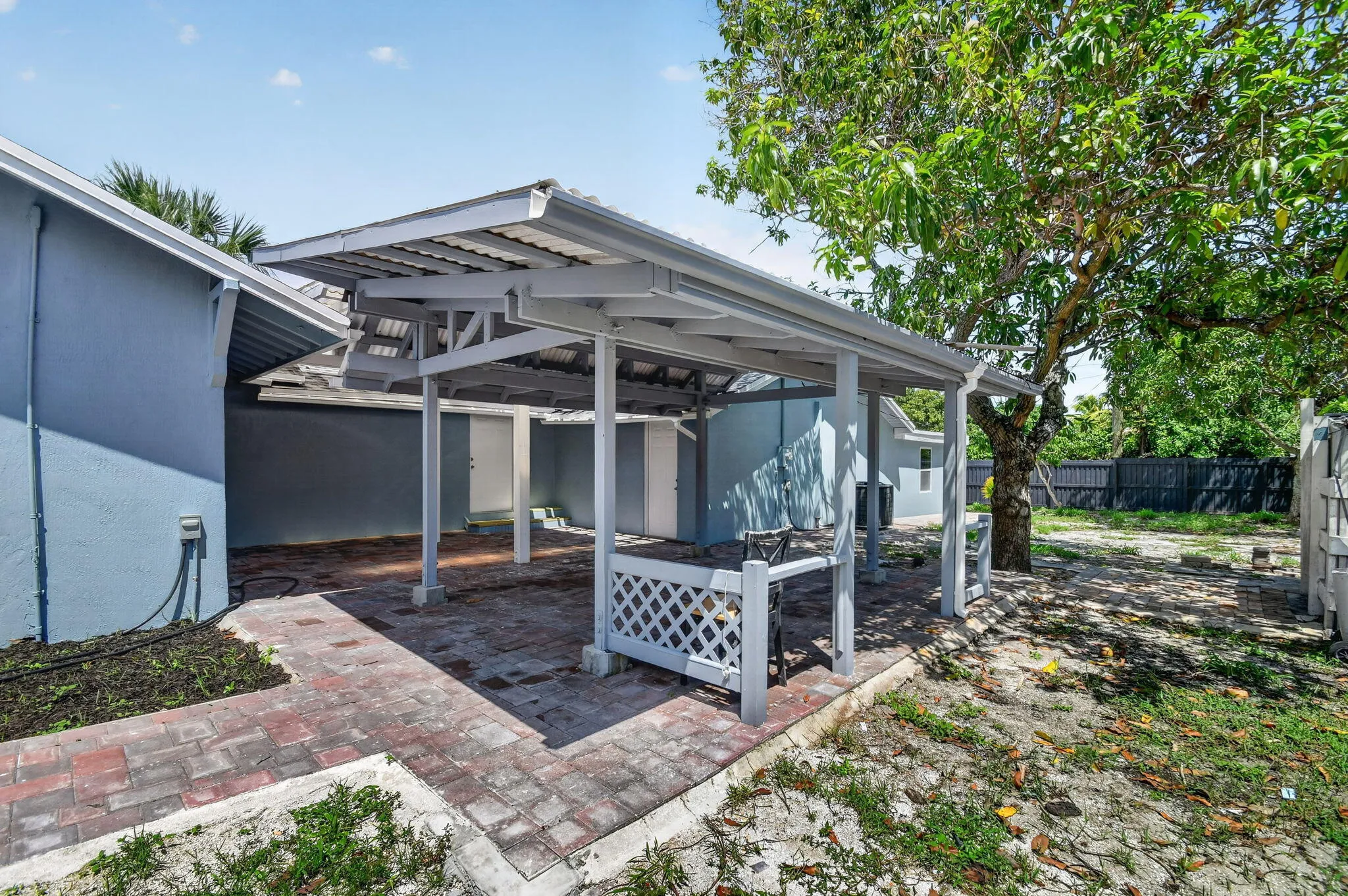 Covered patio structure with white lattice accents, brick paver patio, and mature tree