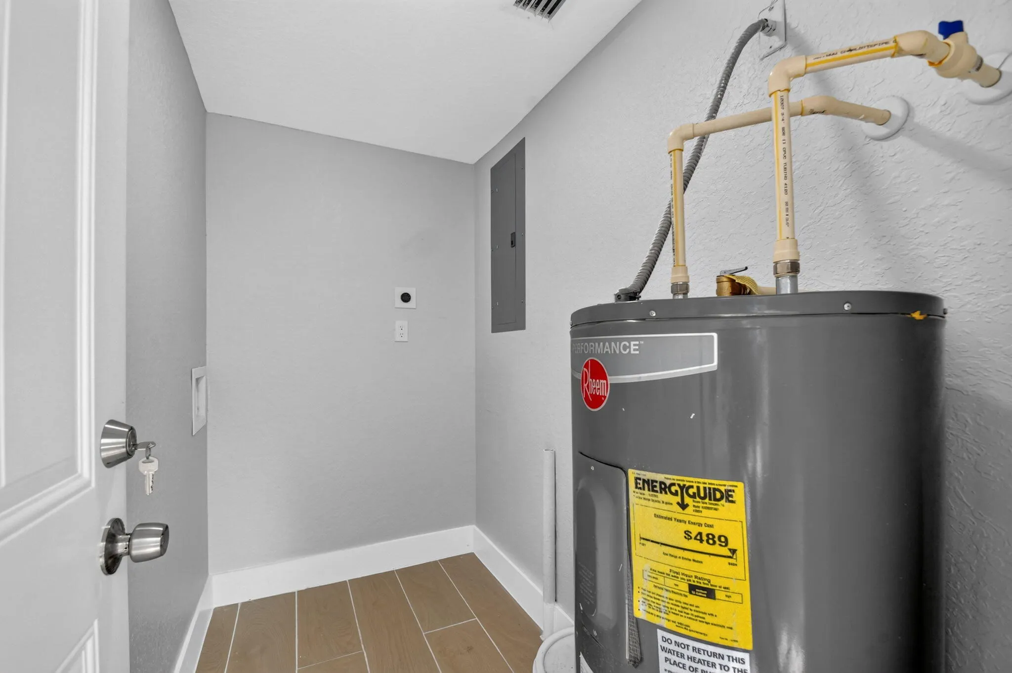 Water heater with visible energy guide, light gray wall paint, and wood-finish flooring