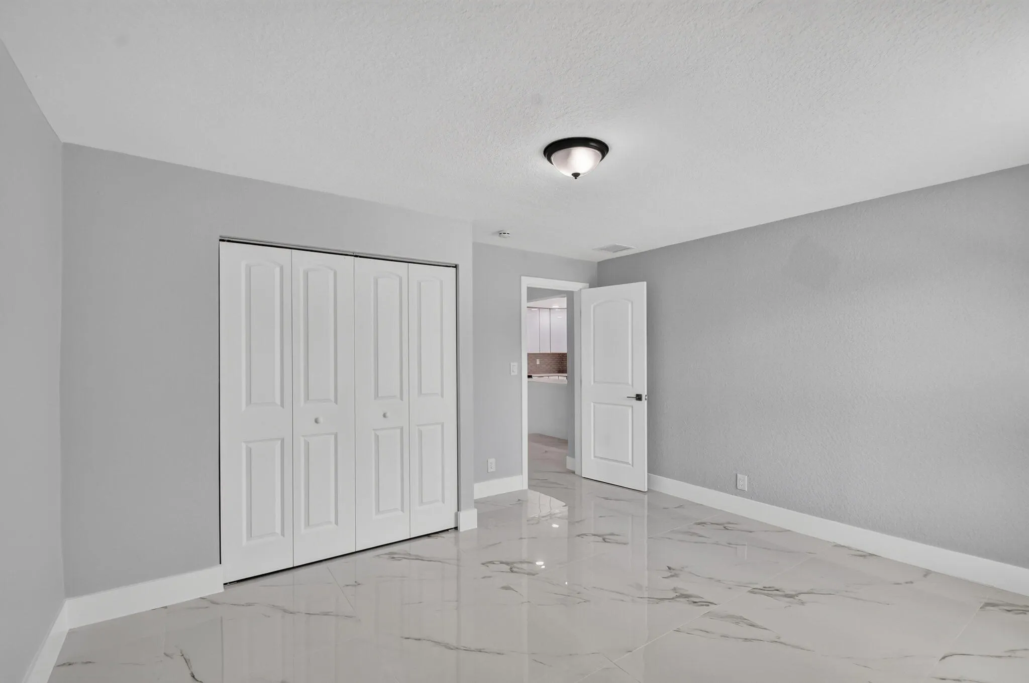 White bi-fold closet doors, white trim, light gray walls, white textured ceiling, and white and gray marble-look tile flooring