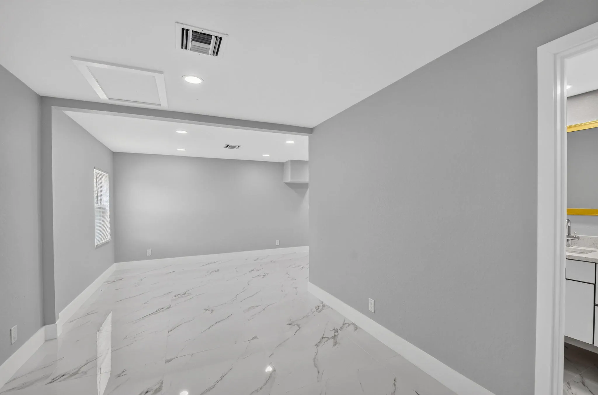 Spacious interior featuring light gray wall paint, large format tile flooring, recessed lighting, and a window for natural illumination