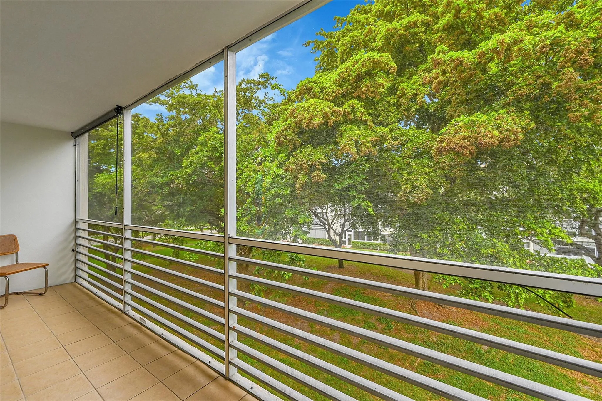 Screened balcony with tiled flooring and a white​​‌​​​​‌​​‌‌​‌‌​​​‌‌​‌​‌​‌​​​‌​​ railing