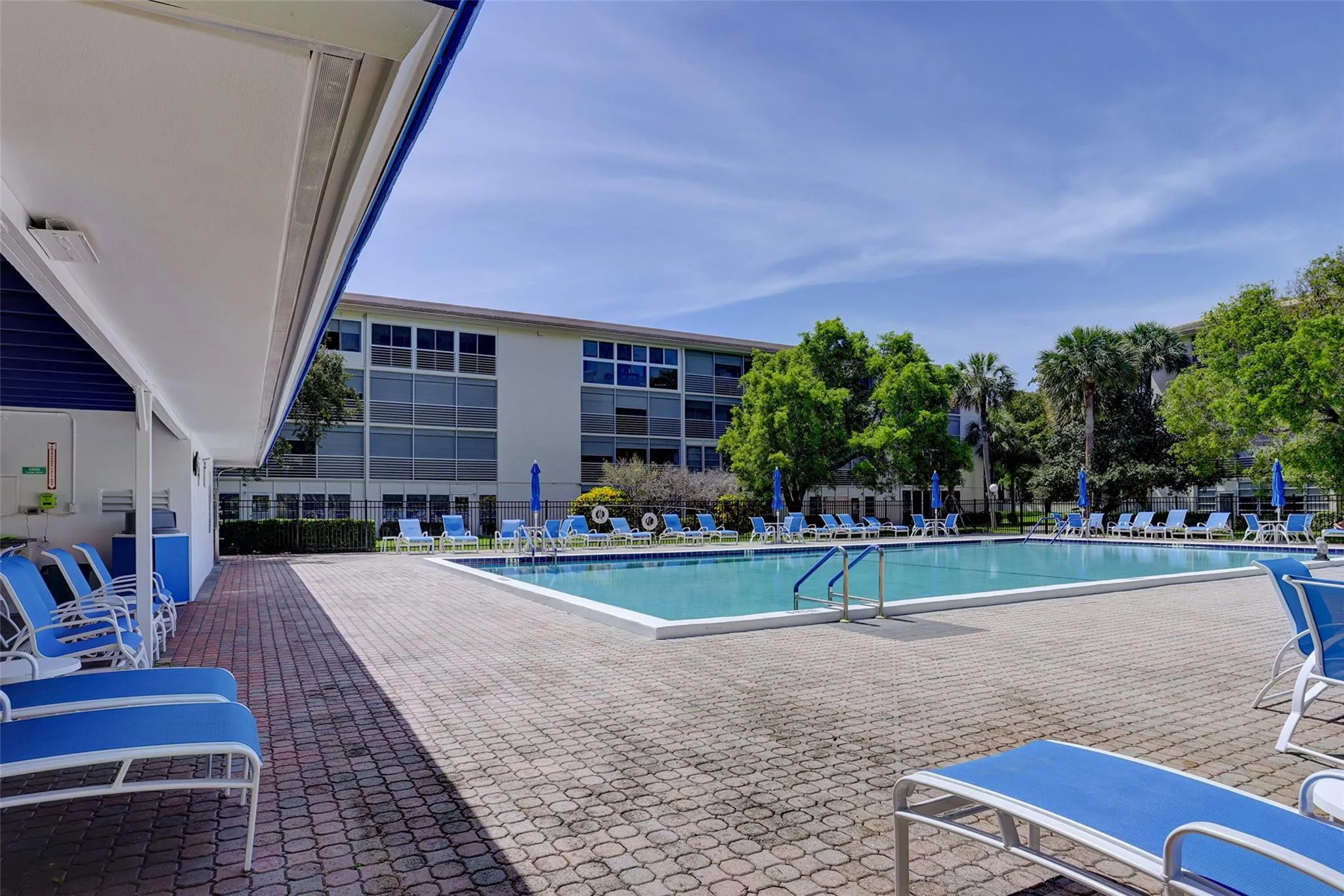 Outdoor swimming pool with integrated steps, surrounded by a paver deck, and adjacent to a covered patio area