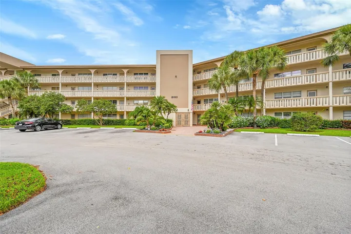 Multi-story building with multiple balconies, a central entryway, and surrounding landscaping
