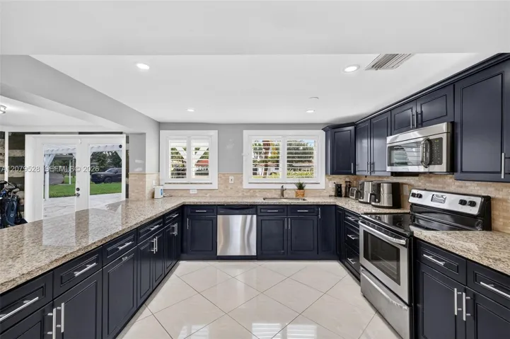 Large bright kitchen w/ windows everywhere, plantation shutters, wood cabinets, stainless appliances and granite counters