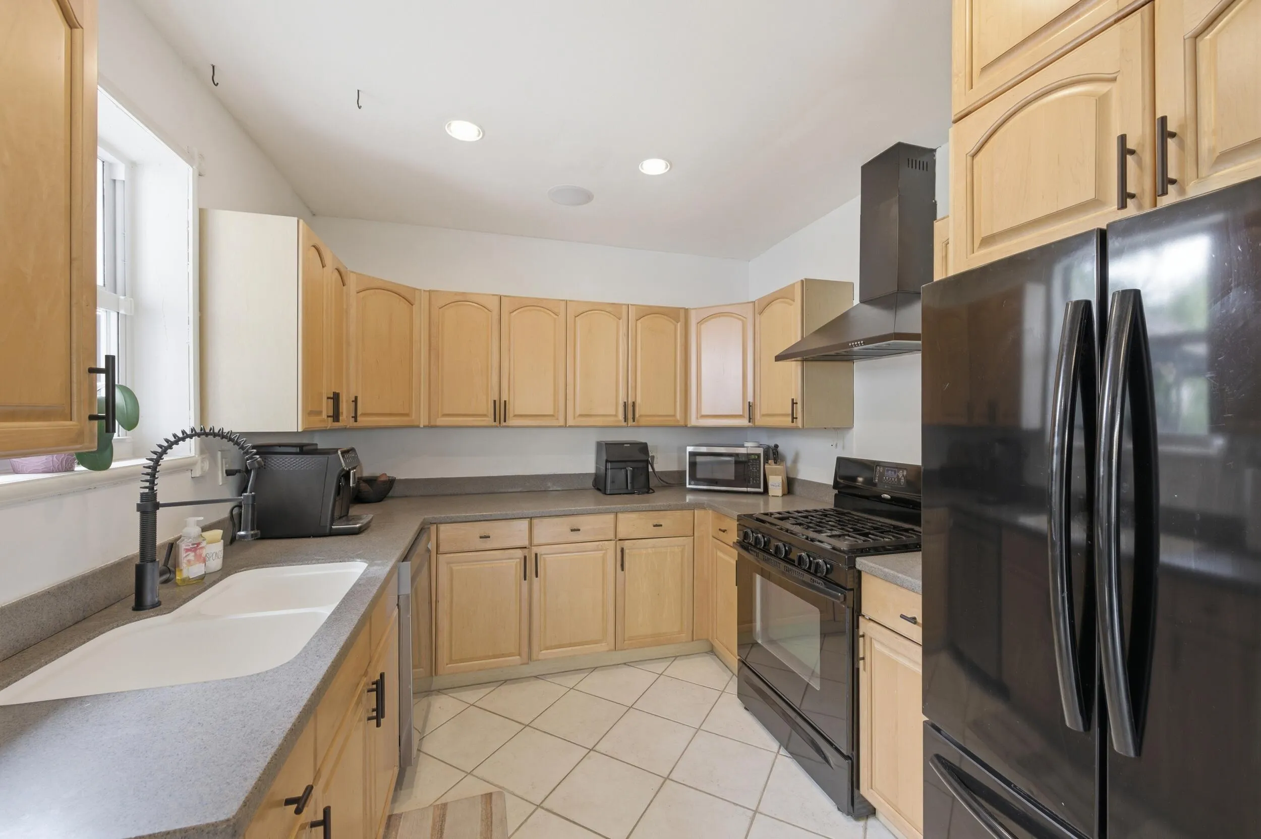 Kitchen featuring light wood cabinetry, recessed lighting, double basin sink with a gooseneck faucet, black appliances, and tile flooring