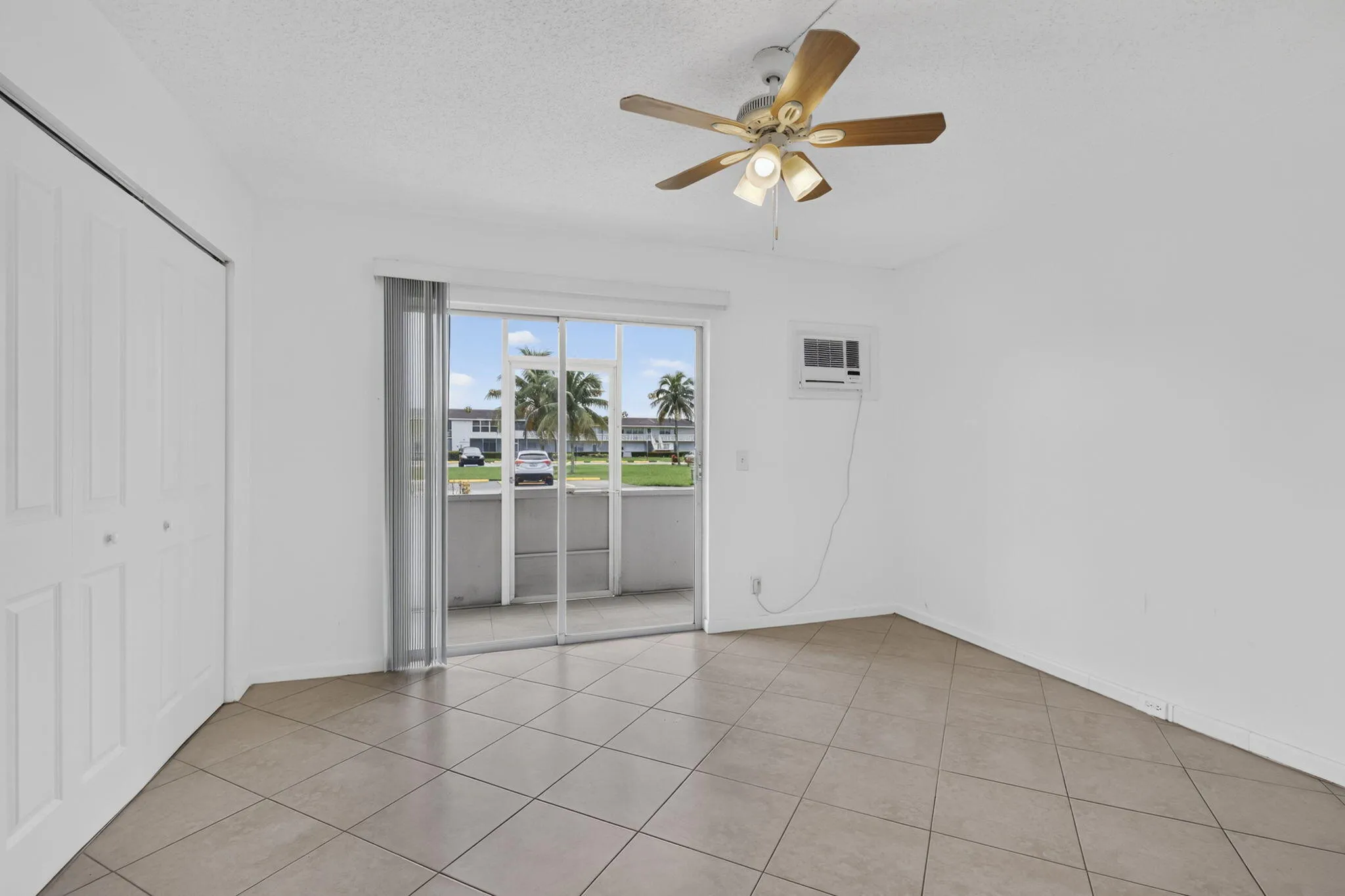 Neutral-toned tile flooring, ceiling fan, sliding glass doors with vertical blinds, and a built-in air conditioning unit