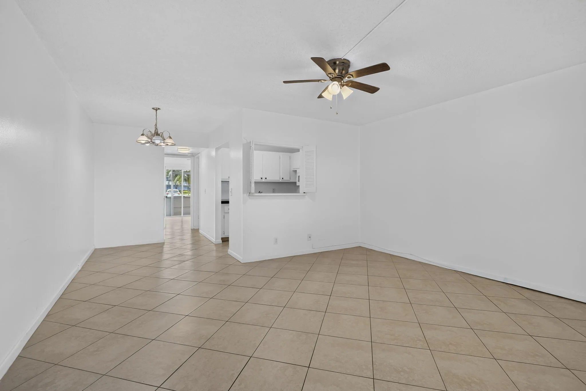 Tile flooring, ceiling fan with integrated lighting, recessed kitchen pass-through, white cabinetry, and pendant light fixture