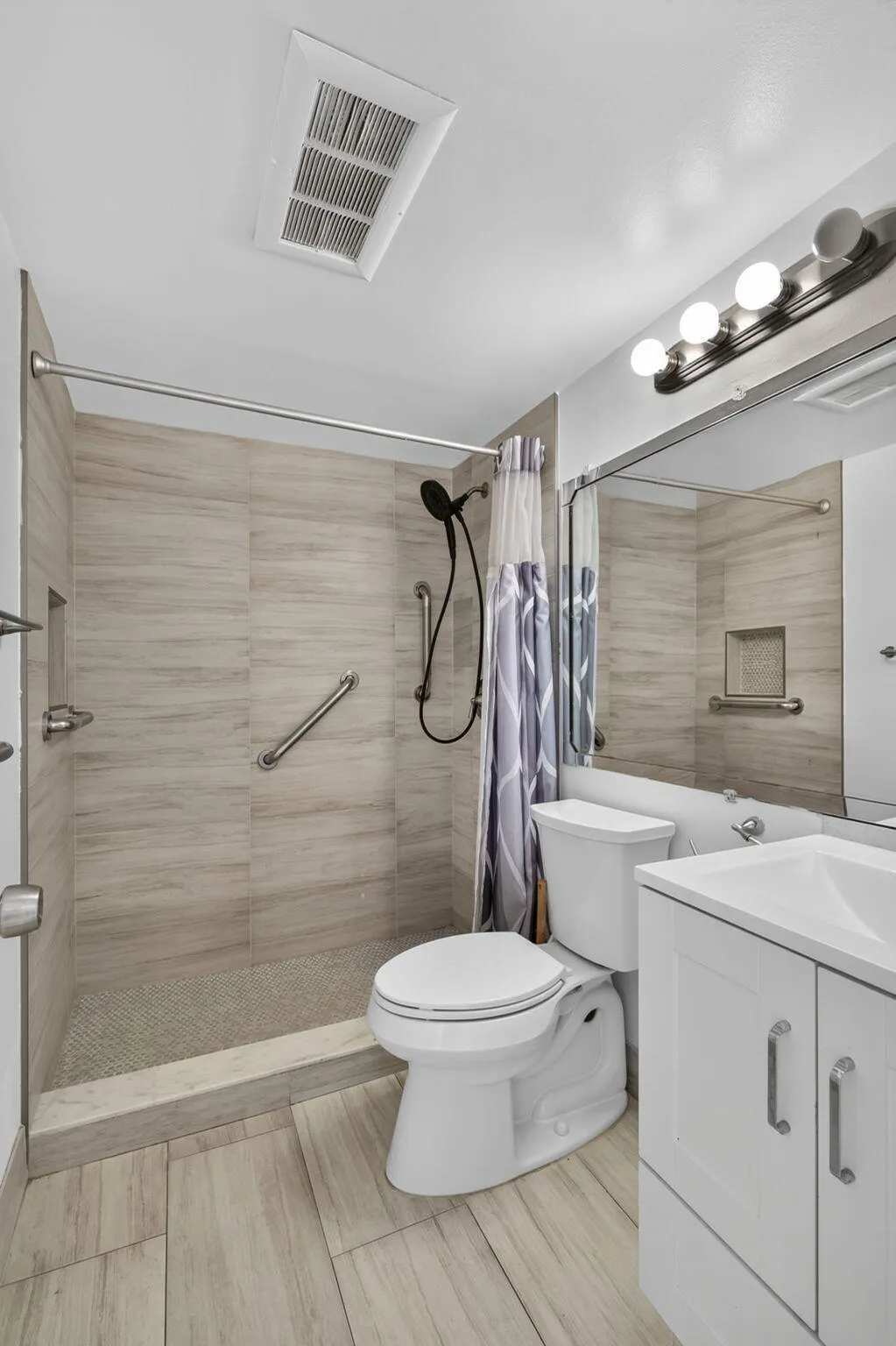 Walk-in shower with light-toned wall tile, white vanity with integrated sink, and wood-finish flooring