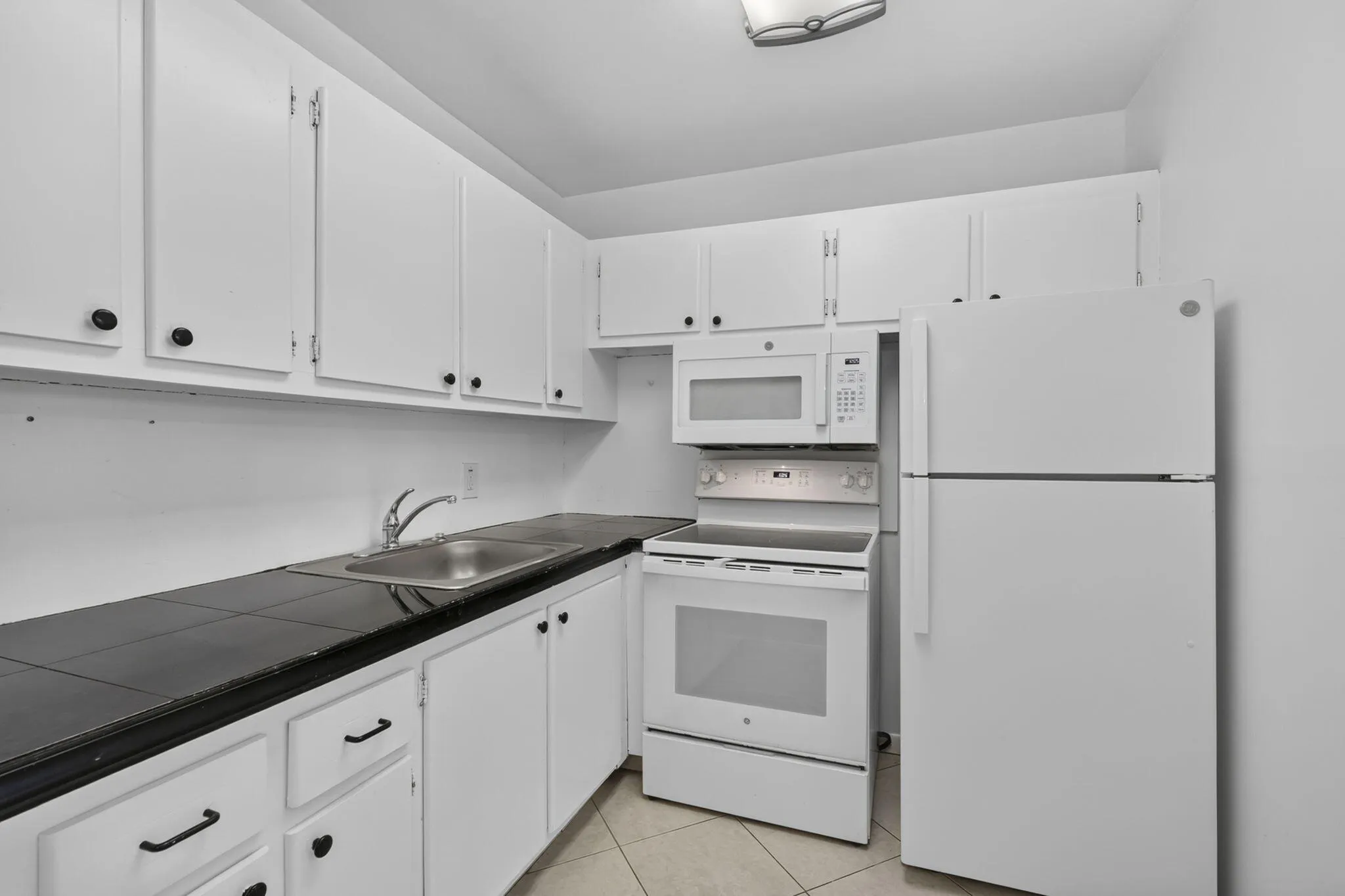 Kitchen featuring white cabinetry, dark countertops, a stainless steel sink, and white appliances including a refrigerator, range, and microwave
