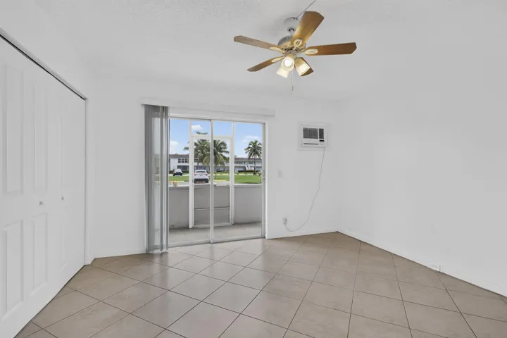Neutral-toned tile flooring, ceiling fan, sliding glass doors with vertical blinds, and a built-in air conditioning unit