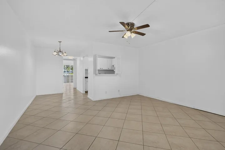 Tile flooring, ceiling fan with integrated lighting, recessed kitchen pass-through, white cabinetry, and pendant light fixture