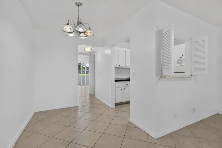 Tiled flooring throughout, recessed kitchen opening with white cabinetry, and a pass-through window with louvered shutters