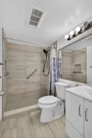 Walk-in shower with light-toned wall tile, white vanity with integrated sink, and wood-finish flooring