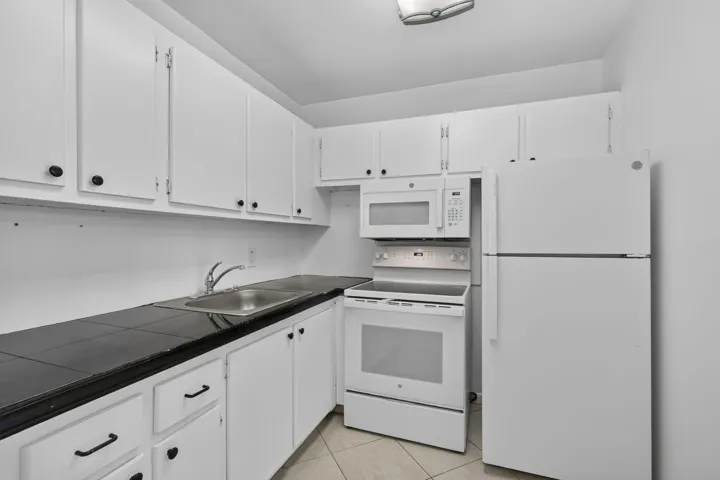 Kitchen featuring white cabinetry, dark countertops, a stainless steel sink, and white appliances including a refrigerator, range, and microwave