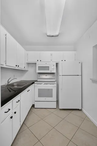 White cabinetry with black hardware, dark countertops, a white electric range, a white microwave, and a white refrigerator