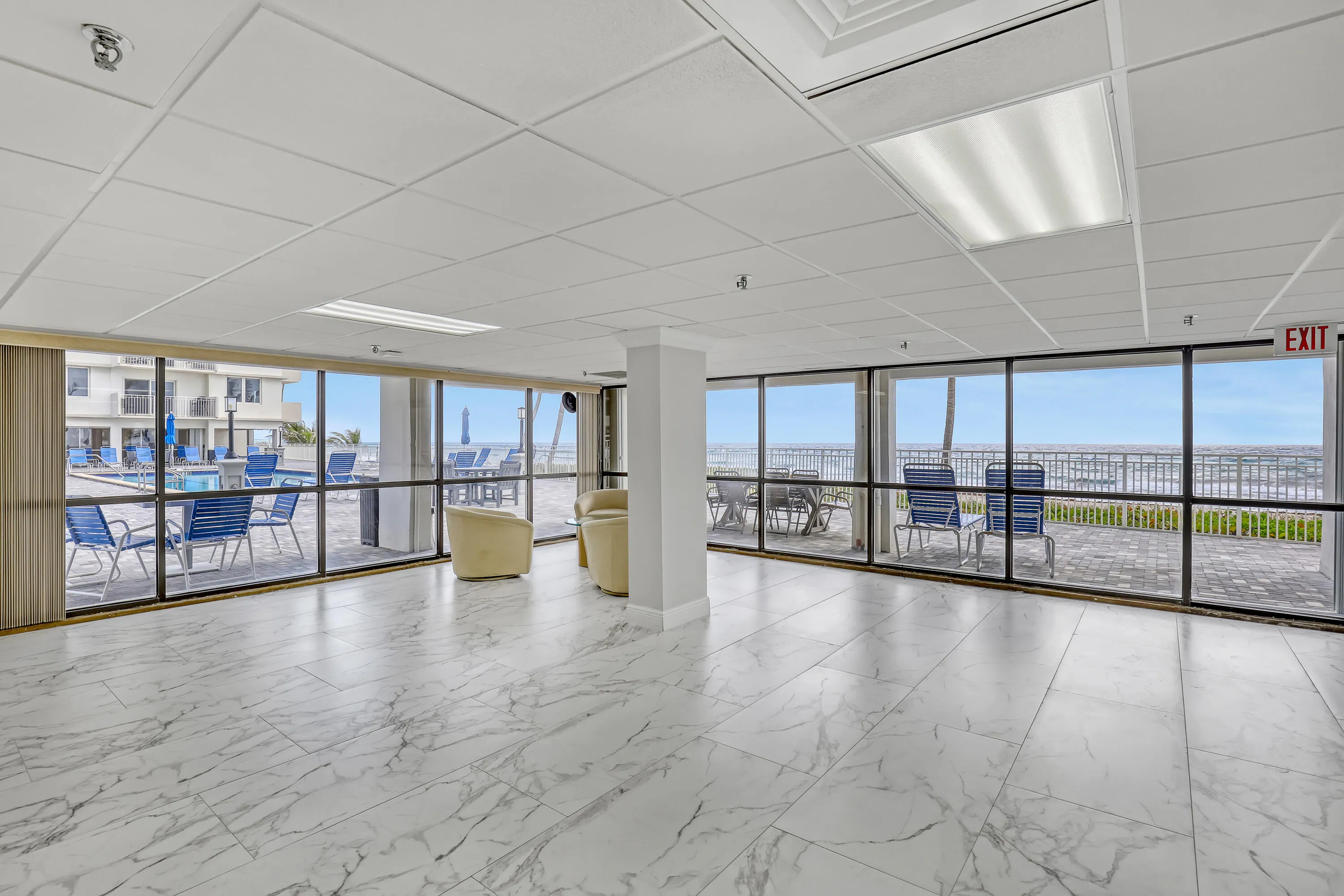 Expansive window wall with ocean backdrop, white tile flooring, recessed and panel lighting, and drop ceiling