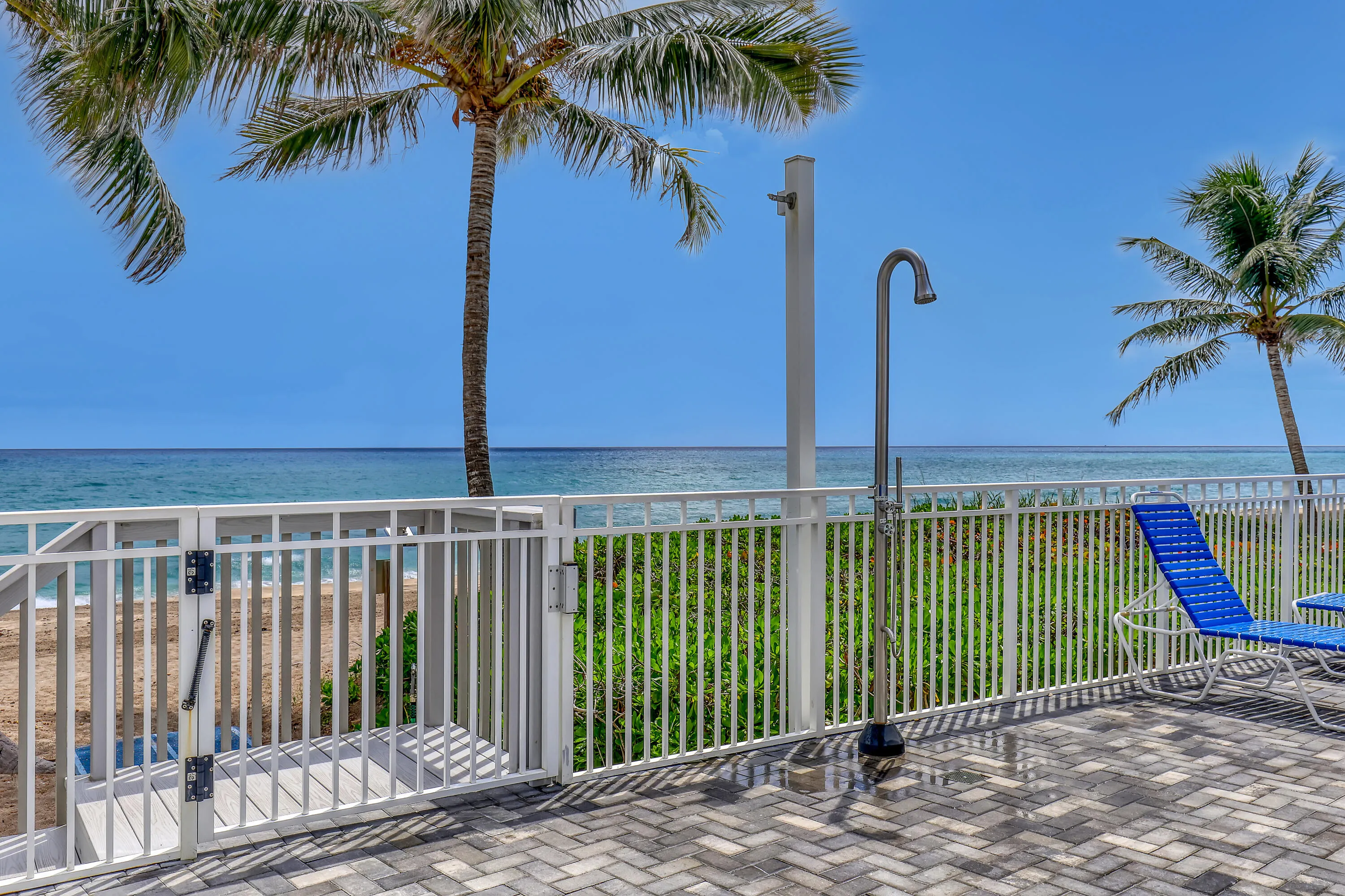 Paved patio with an outdoor shower, white metal fencing, and direct access to the beach