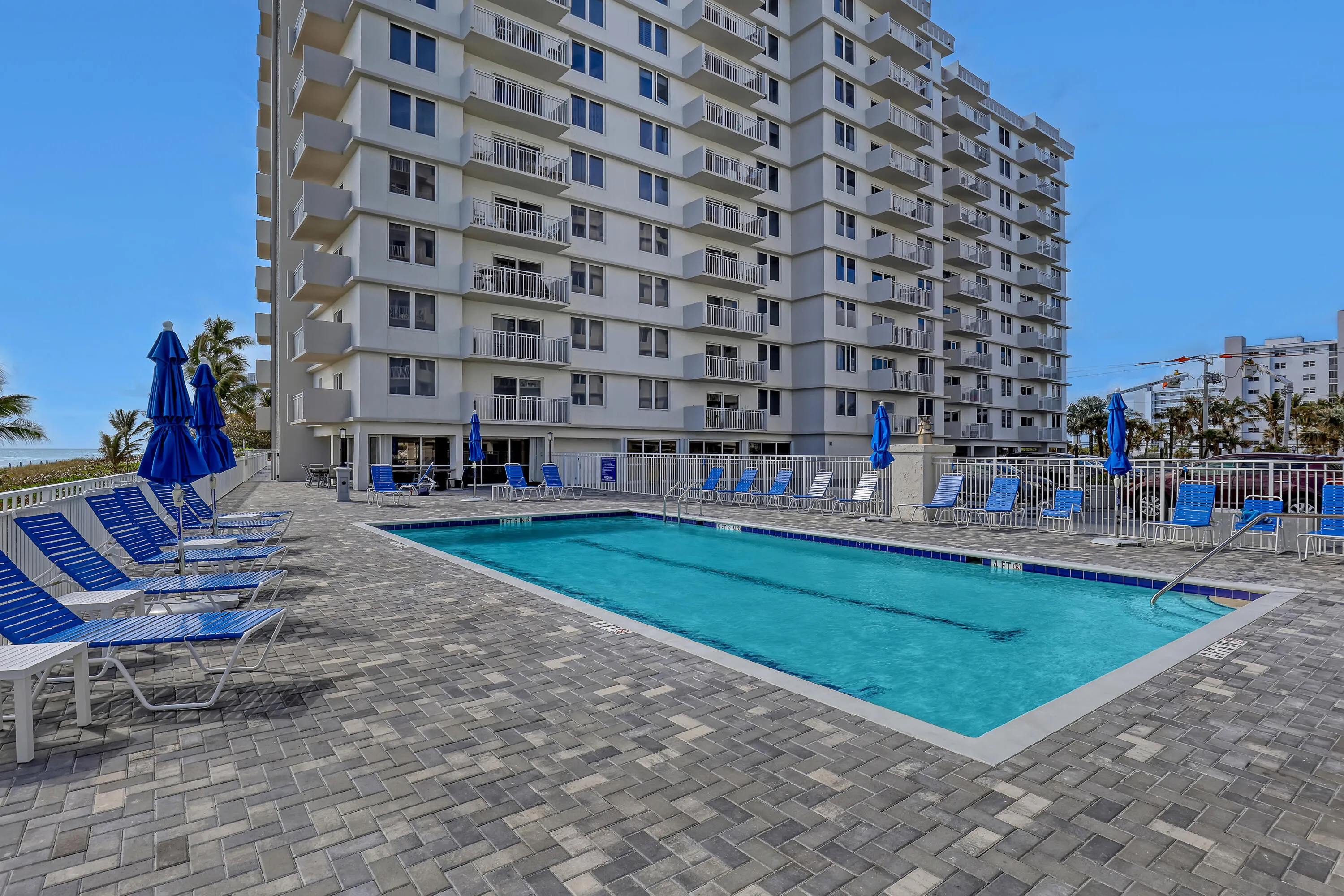 Outdoor swimming pool with integrated steps, surrounded by a paver patio and white fencing
