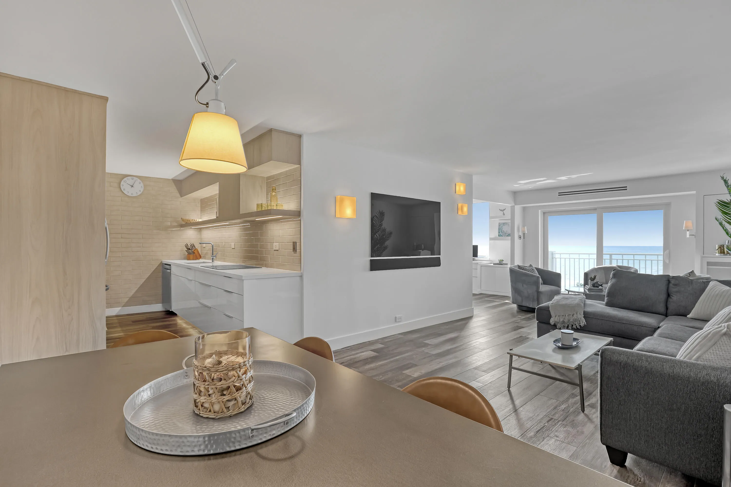 Open-concept living area with wood-finish flooring, a modern kitchen featuring light wood cabinetry, and a living room with expansive sliding glass doors opening to water