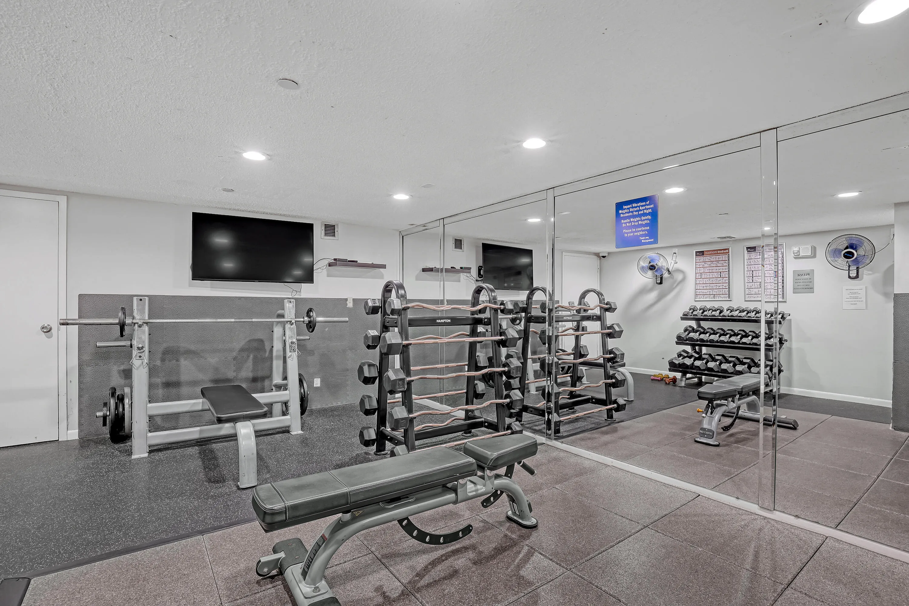 Fitness area featuring mirrored walls, rubberized flooring, track lighting, and wall-mounted televisions