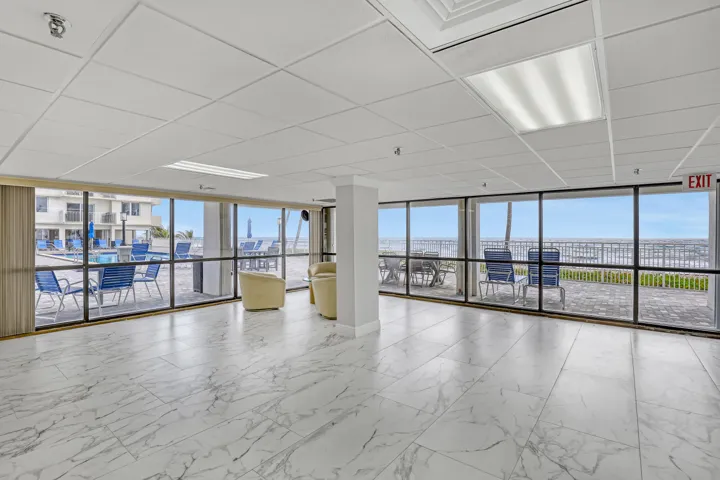 Expansive window wall with ocean backdrop, white tile flooring, recessed and panel lighting, and drop ceiling