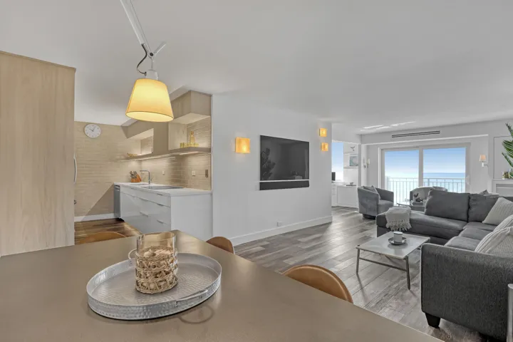 Open-concept living area with wood-finish flooring, a modern kitchen featuring light wood cabinetry, and a living room with expansive sliding glass doors opening to water