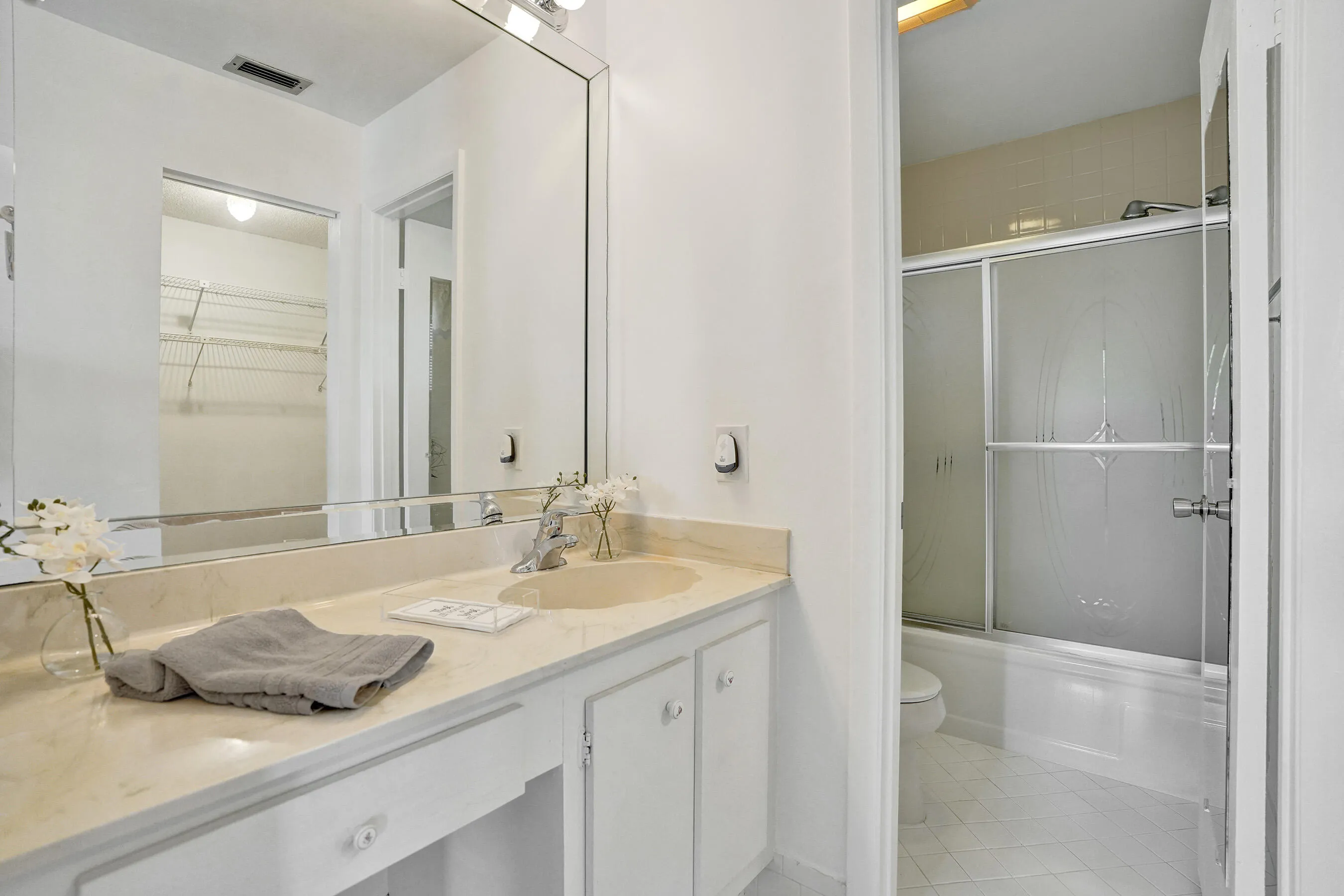 Vanity with integrated sink and stone-look countertop, large vanity mirror, white cabinetry with decorative pulls, and a shower-tub combination with frosted sliding glass doors