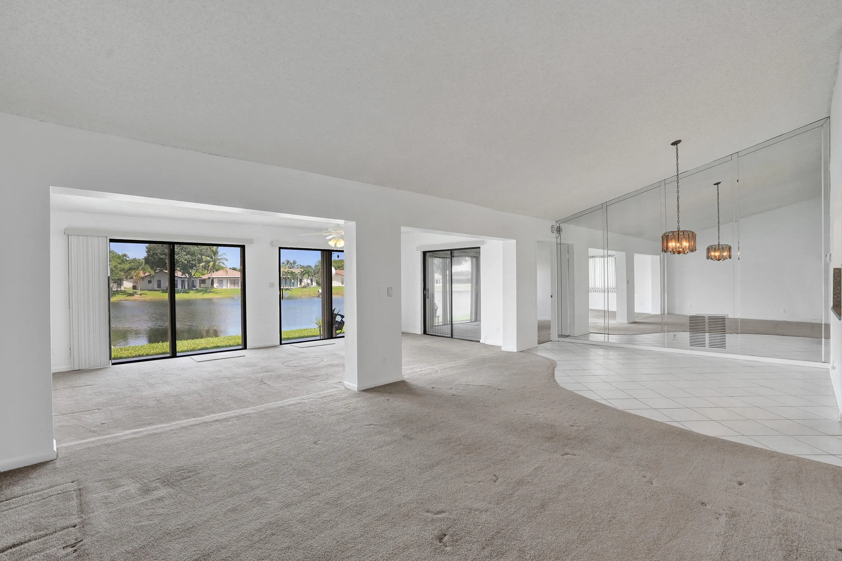 Lakefront sliding glass doors, carpeted living area, tile flooring, mirrored wall, and two pendant light fixtures