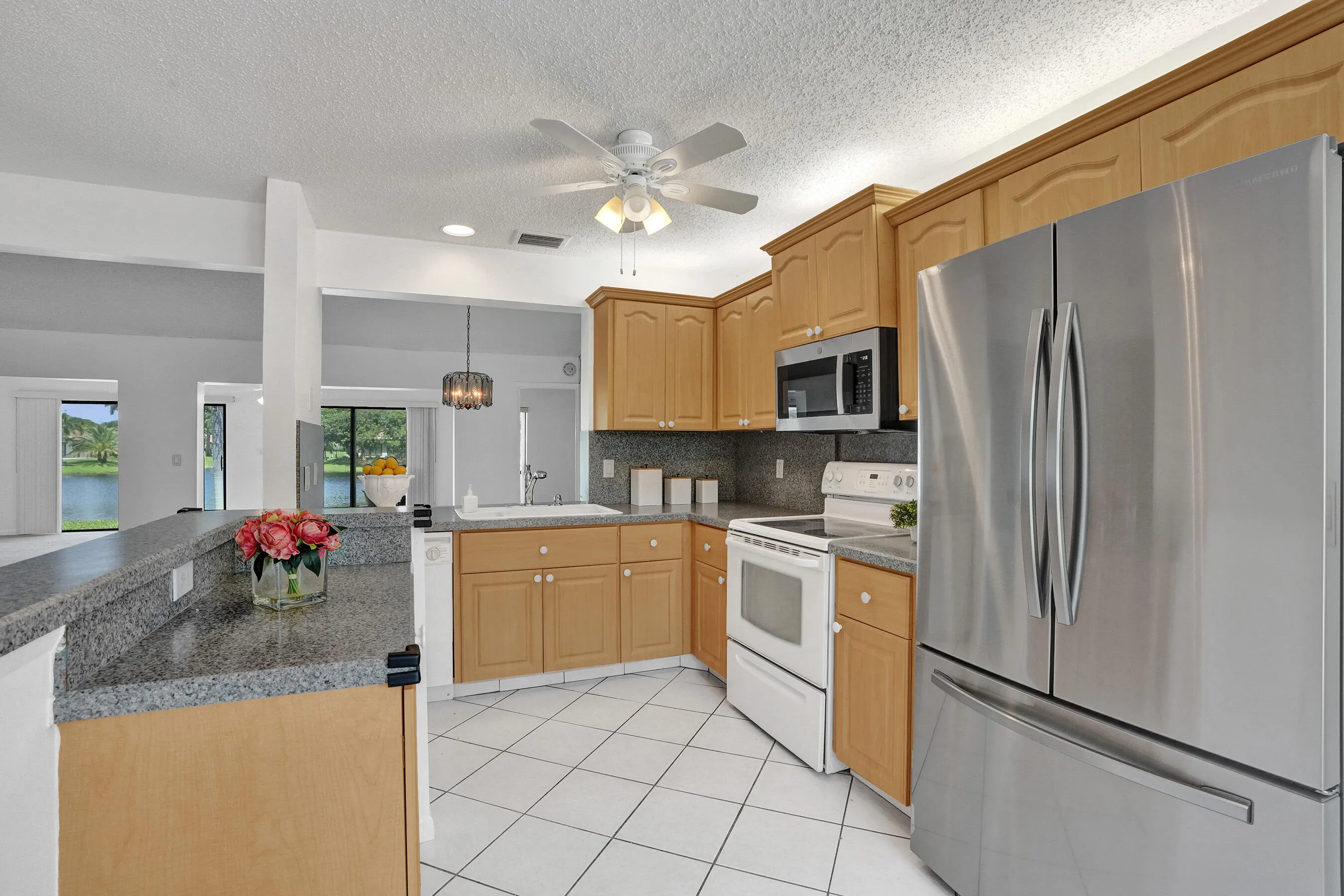 Wood-finish cabinetry, stainless steel refrigerator, white electric range, white tile flooring, and a ceiling fan with integrated lighting